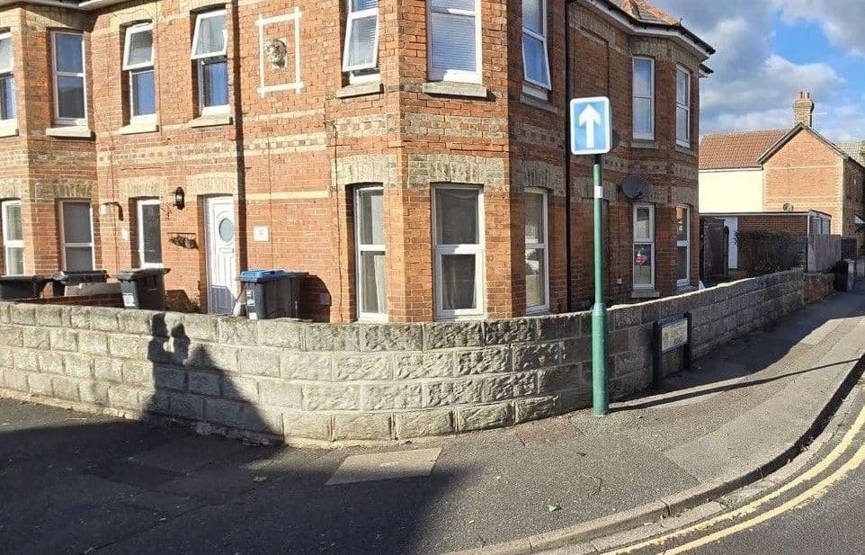 Corner property frontage with overgrown shrubs removed behind the stone wall